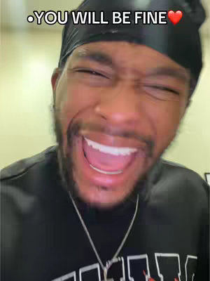 A close-up of a Black man with a black du-rag and smiling widely. The text overlay reads '.YOU WILL BE FINE' with a heart emoji. He wears a black shirt with a word written on it and a silver necklace.