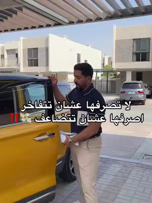 A man in a black shirt and khaki pants stands next to a yellow car, opening its door. Text is overlaid on the image in Arabic. The background includes palm trees, modern houses, and a blue sky.