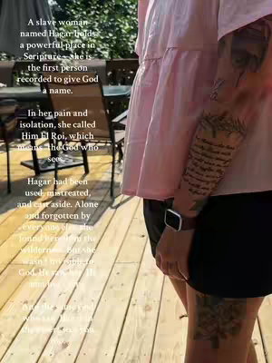 A woman stands outdoors on a wooden deck, with a partially visible background. Her arm is prominently displayed, showcasing a detailed tattoo with script and floral elements. The woman wears a pink top and black shorts. Text overlays on the image explain details about the tattoo.