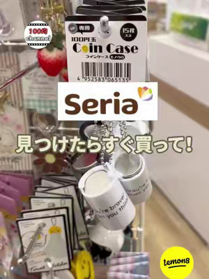The image is a shelf display in a store featuring various coin cases. Prominently displayed is a coin case with a tag labeling it as "100円玉 Coin Case". Below the case is a sign that reads "Seria". The background is blurred, featuring other items on shelves.