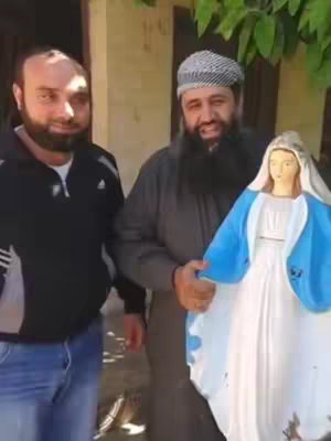 The cover image shows two men and a statue of the Virgin Mary. The man on the left is wearing a black jacket and jeans. The man on the right is wearing a grey robe and a hat. He is holding the statue, which is blue and white.