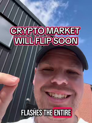 A man in a black cap smiles at the camera against a blue sky and building. Text overlays read "CRYPTO MARKET WILL FLIP SOON" and "FLASHES THE ENTIRE".