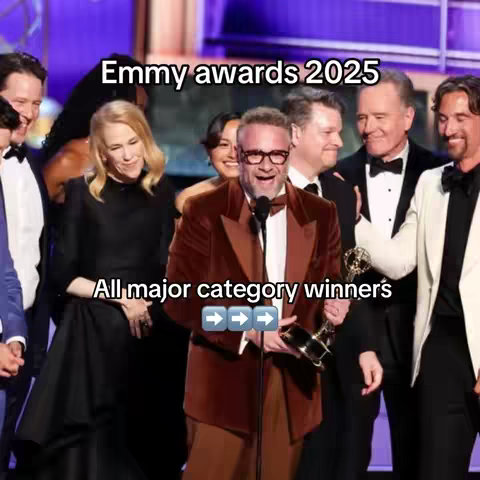 The cover image shows a group of well-dressed people, with a man in the center holding a golden trophy and wearing a brown blazer and glasses. Beside him, there is a woman in a black dress and several other men in suits. The text overlay at the top says "Emmy Awards 2025" with text at the bottom stating "All major category winners" and directional arrows.