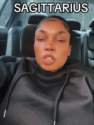 The cover image shows a close-up selfie of a woman inside a car, seated in the back. The woman, with dark hair and a black hoodie, has her eyes closed and mouth slightly open. Above the woman's head, the text 'SAGITTARIUS' is placed in a rectangular, white font. The background is a blurry view of the car's interior and the headrest.