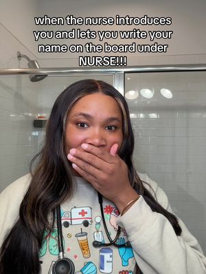 A woman is shown in a selfie-style video, covering her mouth with her hand while looking directly at the camera. Above her, text is overlaid on the image. The background includes a shower setting with white tile.