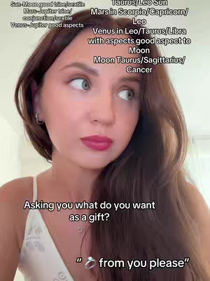 The cover image is a selfie-style shot featuring a woman. The woman, with long dark hair, is positioned centrally in the frame, looking slightly off-camera towards the right. The background is softly blurred, suggesting an indoor setting. The woman is wearing a white top, and she has lipstick. A text overlay with astrology details covers a portion of the image. The image composition is typical of a social media post, with the focus on the woman's face and the overlaid text as a hook.