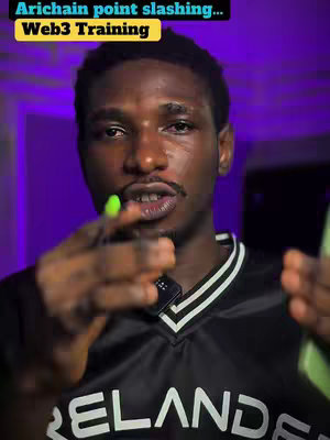 A man is in the center of the image. He has dark skin, short black hair, and is wearing a black shirt with white stripes on the collar. The background is a gradient from purple to dark gray. There is text on a yellow background in the top left, and the man is holding what appears to be a pen in one hand and has his other hand near his face. The lighting is focused on his face.