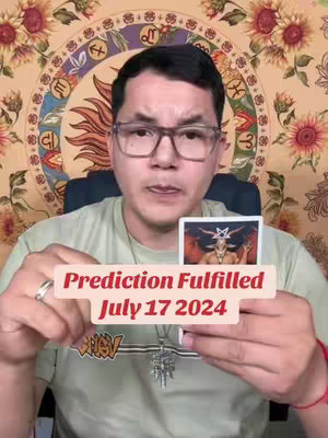 A man with glasses holds up a tarot card in front of him, with text overlaid that reads 'Prediction Fulfilled July 17 2024'. He is in a room with a decorative background.