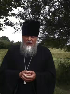 The cover image features an older man in religious garb. He is the central figure, positioned in front of a blurred outdoor setting that includes foliage. The man has a long, white beard and wears a tall, black hat. He's clad in a black robe, with a silver necklace. He appears to be speaking or singing, with his mouth open. The background is a muted green, providing a natural, slightly out-of-focus backdrop.