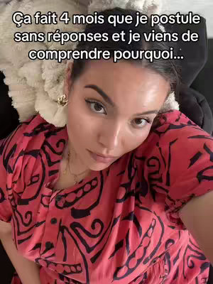 A selfie-style shot with the creator looking directly at the camera. The background is blurred but appears to be a bed or couch with a cream-colored pillow. The creator wears a red and black patterned top and gold earrings. She has a neutral expression. Text overlay at the top.