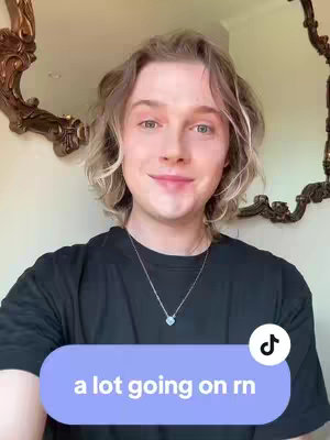 A young person with light hair and a black t-shirt smiles subtly at the camera in a well-lit space. Behind them is a decorative mirror. A purple text box at the bottom says 'a lot going on rn.' A TikTok logo is in the bottom right.
