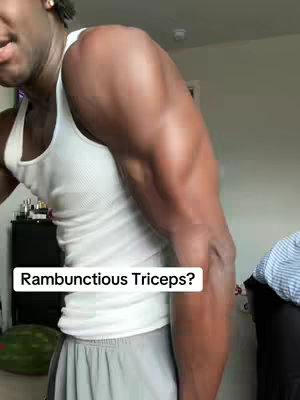 A man with dark skin, wearing a white tank top and gray shorts, flexes his right arm, highlighting his triceps. A text overlay asks "Rambunctious Triceps?" The background is a room with a partially visible watermelon. The lighting is natural, and the focus is on the man's arm.