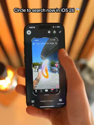 A person holding an iPhone, showing the screen with a circular search highlighting a feature of iOS 26. The background shows a wooden structure, and text overlays the top of the phone's screen.
