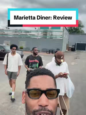 The cover image is a selfie-style shot with the main focus on a person in the foreground wearing black sunglasses, with three other individuals slightly behind. The background includes a building and a car. A text overlay states the name of the restaurant and the video is a review.