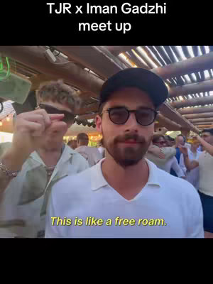 The cover image shows two men in an outdoor setting. The man in the foreground closest to the camera is wearing a white collared shirt, a watch, and dark sunglasses. He has a beard and is looking directly at the camera. The man behind him has lighter hair and is looking to the side while partially obscured by the foreground man. A text overlay reads, "This is like a free roam."