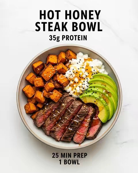 A close-up shot of a white bowl filled with a meal, set against a minimalist white background. The bowl is divided into sections, showcasing various components. On the left, there are small, orange cubes resembling cooked sweet potatoes. Adjacent to these, a generous portion of cottage cheese with some dark specks (likely seasonings). To the right, a few slices of avocado are presented. At the bottom, the bowl displays sliced steak. It's neatly arranged and drizzled with hot honey.