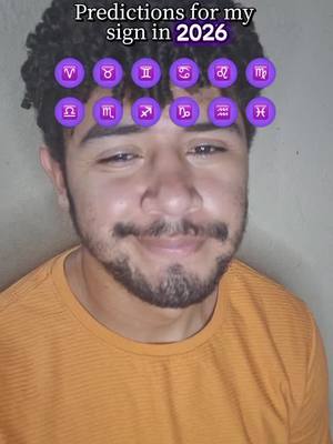 A man with short curly dark hair and a goatee smiles. He is wearing a bright orange t-shirt, and has overlaid zodiac signs floating above his head. Text in the top left corner reads, "Predictions for my sign in 2026."