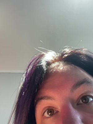 A close-up shot from the forehead down, revealing a person's dark hair and a portion of the face, with bright lighting from above on the hair. The focus is on the top of the head and the beginnings of the eyebrows and eyes.