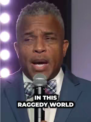 A close-up shot of a man speaking into a microphone. He is wearing a suit and a bow tie. Text overlay is added at the bottom.