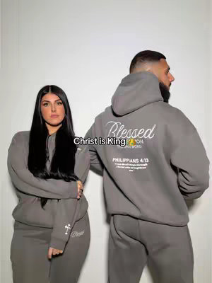A photo of a woman and a man wearing matching grey hoodies and sweatpants. The background is plain white. The woman is on the left, gazing at the camera. The man, on the right, has his back to the camera, with just his face visible, looking off to the side. 'Christ is King' is written in the image in white.