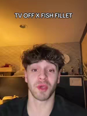 A selfie-style video with a young man in the foreground, slightly off-center. He's looking toward the camera with a slightly parted mouth, possibly speaking. Behind him, the background is softly lit with warm tones, suggesting an indoor setting. Above him, a text overlay states 'TV OFF X FISH FILLET' in a bold, sans-serif font.