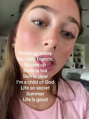 A close-up shot of a young woman looking at the camera, with text overlays in white appearing on the image. The woman has long brown hair, fair skin, and a pink shirt. Her eyes are wide with makeup, and her lips are slightly parted. Additional background elements include hints of a room, which looks like a living room.