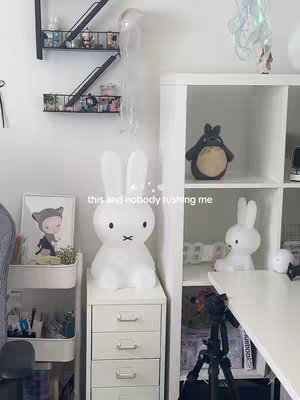 A cozy room with a white desk and shelves is the focal point. A large white Miffy lamp sits atop a white dresser, and a small Miffy figurine is visible on a shelf. Other decorative elements in the room include Ghibli-themed items such as a Totoro plush and a Ponyo picture.