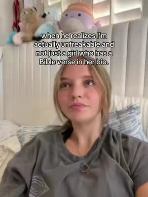 A young woman is shown from the chest up, gazing slightly off-camera with a thoughtful expression. Behind her, a fluffy white headboard is visible, topped with a variety of plush toys. Text overlays, in a sans-serif font, explain the context of the video.