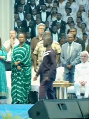 The image captures a moment during a Christian healing event. In the foreground, a man, seemingly the focus, walks forward while in the middle distance are other people. In the background is a crowd of people. The lighting appears to be natural and bright.