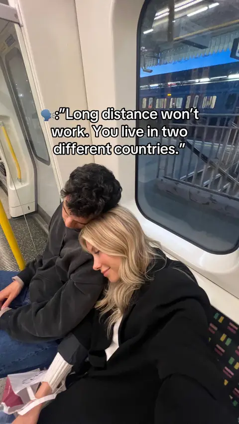 A couple sits close together on a train. The woman is resting her head on the man's shoulder while they are in transit through the train station.