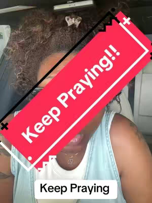 A selfie-style video cover image featuring a woman with curly hair. The woman is seen from the chest up, wearing a light blue top and glasses. A large red rectangle with white text overlayed on it says 'Keep Praying!!' in bold, sans-serif type. Beneath the red rectangle is a white rectangle containing 'Keep Praying.'