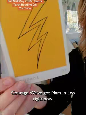 A person holds a tarot card with an image of a lightning bolt on a yellow background. The person is partially visible.