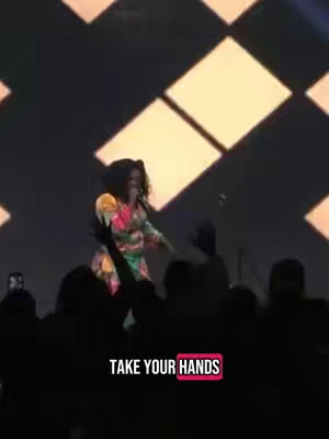 The cover image shows a woman on stage, gesturing with her hands. She is wearing a colorful dress and is in front of an audience, as suggested by the silhouettes in the foreground. The background has diamond-shaped light fixtures.