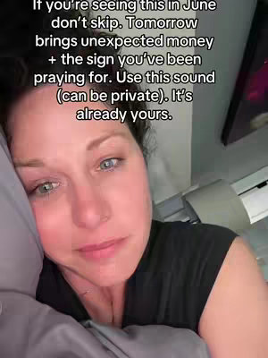 A selfie-style shot of a woman in bed, looking slightly to the side with what appears to be tears in her eyes. She's resting on a gray pillow, and the lighting is soft. Text is overlaid on the image.