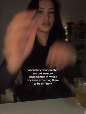 The image captures a young woman in a dimly lit setting, likely indoors. Her face is central, with her features slightly blurred, and she's positioned in front of what appears to be a dark background. The overall tone is moody.