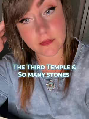 A close-up selfie of a woman with light skin and brown hair. She has fair skin, visible eye makeup, and is looking at the camera with a slightly downward gaze. The image includes overlay text in a teal-blue color, stating "THE THIRD TEMPLE & SO MANY STONES." She's wearing a blue shirt and a necklace with an oval pendant, and the image is well-lit overall with a soft focus.