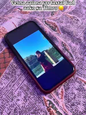 A smartphone displaying a video of a couple embracing against a bright sky background rests diagonally on a patterned bedspread. The phone’s screen is the focal point.