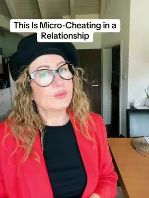 The image features a woman with curly blonde hair, wearing large-framed glasses, a black beret, a black top, and a bright red blazer. She is turned slightly to the side, looking towards the camera. The background includes an interior space with a door, and a desk.