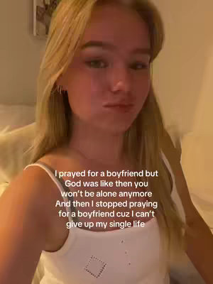 A selfie-style video shot featuring a young woman with long blonde hair. She's in a room with warm lighting, likely indoors, wearing a white tank top. The primary focus is on her face, where she has a slight pouty expression and her eyes are looking towards the camera. Text overlays the image, outlining a narrative.