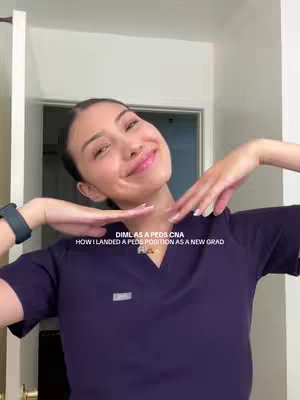 A young woman with dark hair and a soft smile is featured in a selfie-style shot. She is dressed in a purple scrub top, with her hands gesturing near her face. Text overlays are present at the bottom and top. The background is a neutral-colored room with a partially visible door and white walls, providing a clean and focused aesthetic.