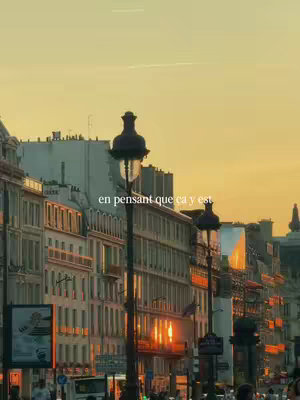 An urban cityscape at sunset. Tall buildings line the streets, with prominent street lamps in the foreground. The sky transitions from golden to a soft orange as the sun sets. Text overlay is present at the top.