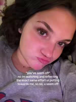 A selfie-style shot featuring a young woman. She has dark hair, and her face is close to the camera. She has full lips and a neutral expression. Overlayed on the image is white text that expresses a feeling. The background is out of focus suggesting an interior setting.