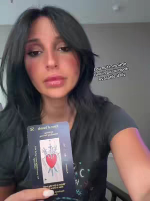 A woman with long black hair is the central focus, looking at the camera and holding a tarot card. On the right side, there is a text overlay with information about booking. The background is blurred.