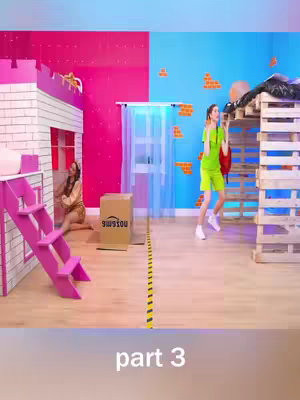 The image showcases a split environment with a room divider. On the left, a miniature house is constructed with pink stairs and a seated woman. The right side features a wooden structure with a woman in a lime green outfit captured mid-action, potentially dancing or reacting. The color scheme is playful, with pink and blue walls, and a yellow box.