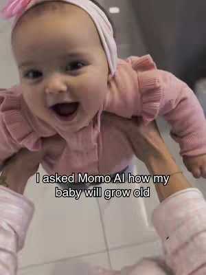 A smiling baby is held up in the air by two visible arms. The baby has an open mouth and is wearing a pink top and white headband. Text lays at the bottom of the screen.