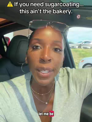 A selfie-style video shows a Black woman inside a car, likely the driver's seat. She is wearing sunglasses pushed up on her head, with a light-colored top, and multiple necklaces. The background shows an out-of-focus environment with other cars. The image has text overlays in yellow text with a black outline and in red.