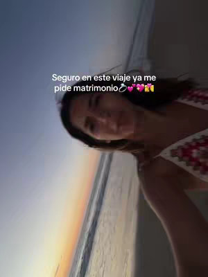 A selfie-style shot of a woman at the beach. She is looking towards the camera, with a beach and ocean landscape visible in the background. Text overlay with the woman wearing a crochet top.