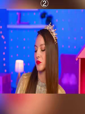 The cover image features a woman in a room with blue walls and small pink squares. She looks down, her expression solemn. She's wearing a gold, shimmering top and a princess-like crown on her head. Her lips are vividly red. The background hints at a dollhouse or similar themed design. The top section of the image has a brown border and the number 2 in a circle.