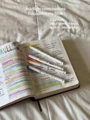 An open Bible lies on a white bedsheet, with several colorful highlighters placed on top. The Bible is open to a page with text highlighted in various colors, including yellow, pink, and blue. The text overlay says "mildliner combinations I've used in my Bible", followed by specifics.