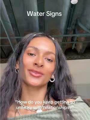 A medium shot shows a woman with dark hair and light skin looking towards the camera with a slight smile and tongue out. The overlay text that is on the cover image reads 'Water Signs'. The background has a dark color and appears to be a ceiling.